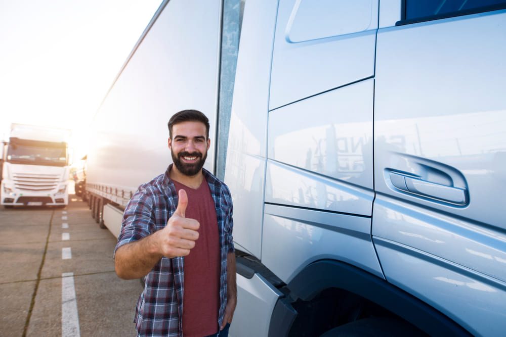 A truck driver showing thumbs up, and he is standing near to a truck